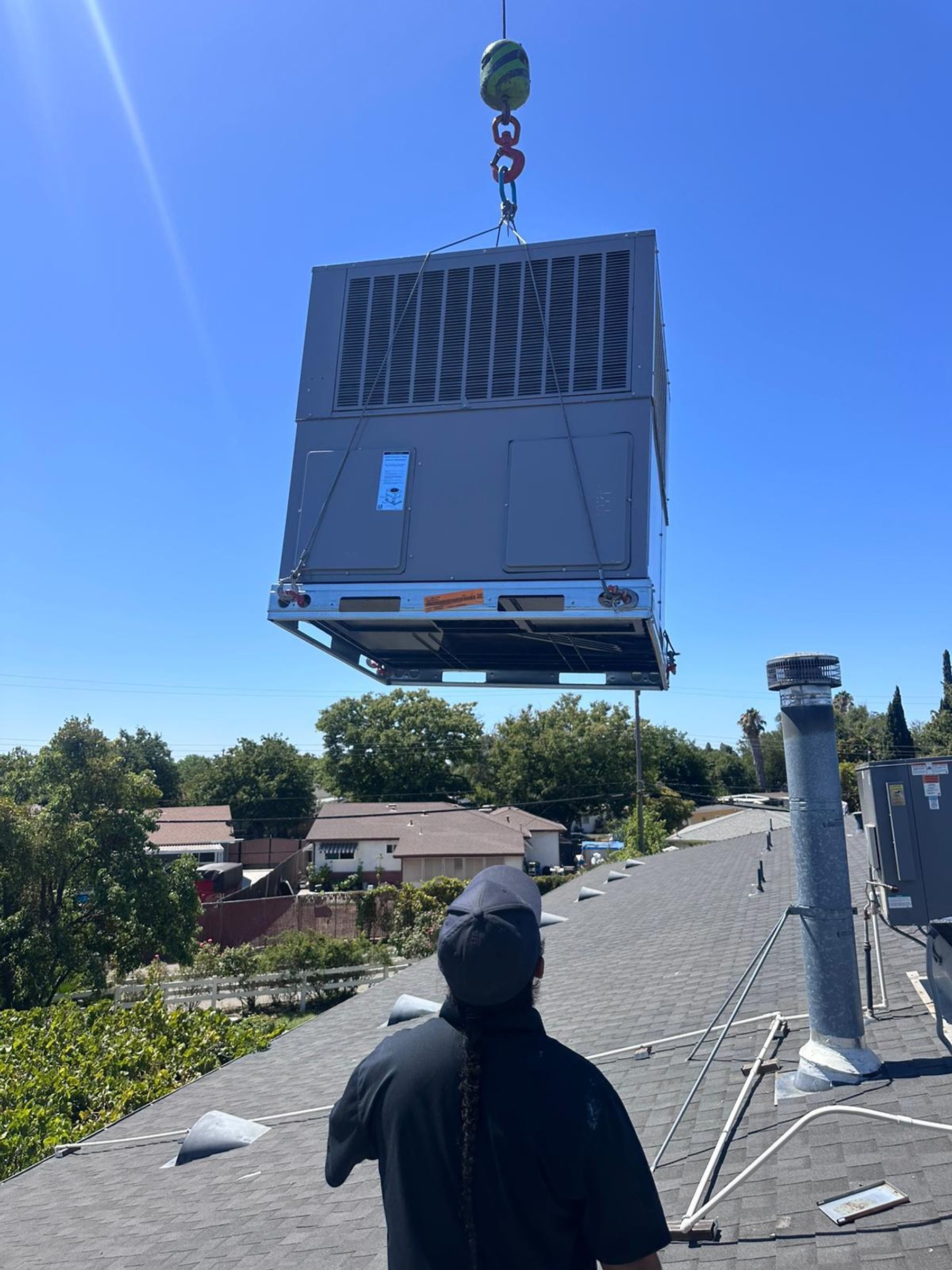 A crane hoisting a commercial rooftop packaged HVAC unit onto a building with an RB HVAC technician guiding placement.