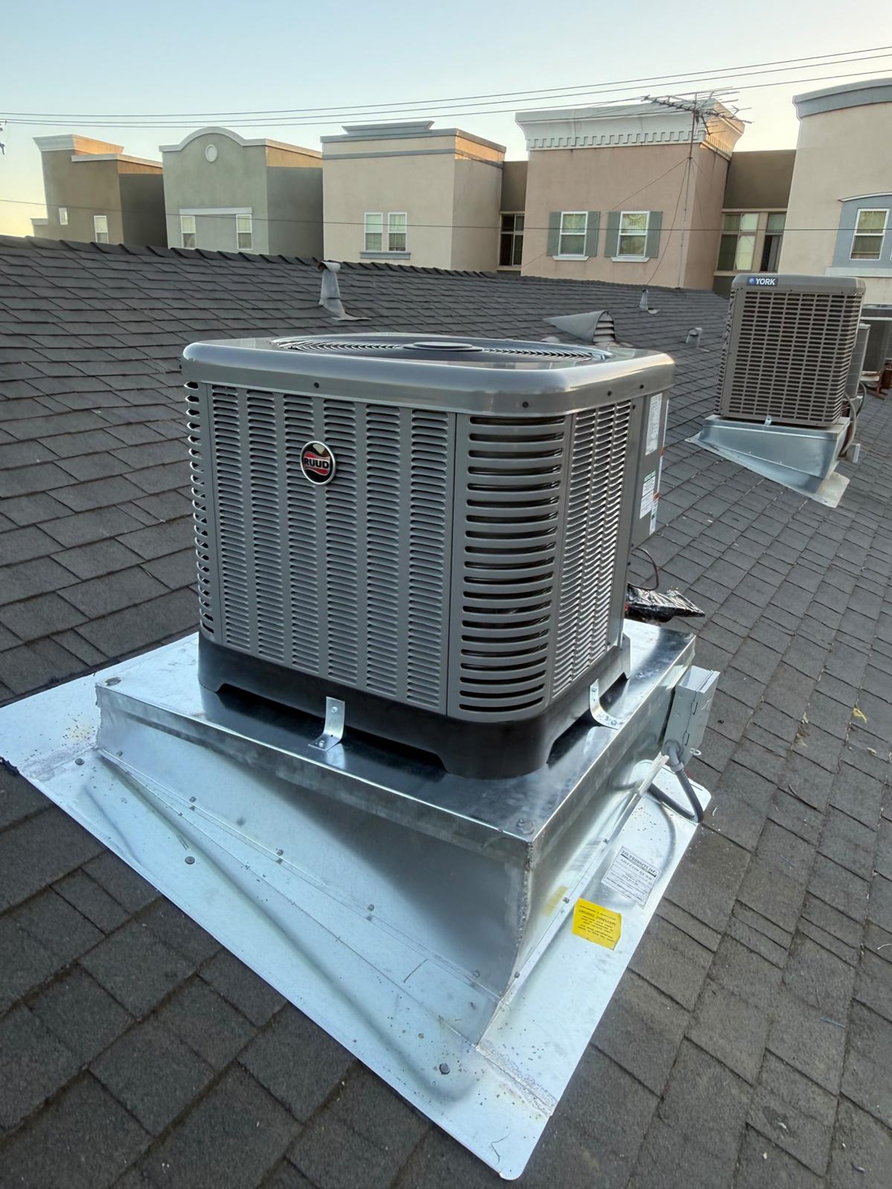 A Ruud residential condenser mounted on a pitched-roof curb transition stand.