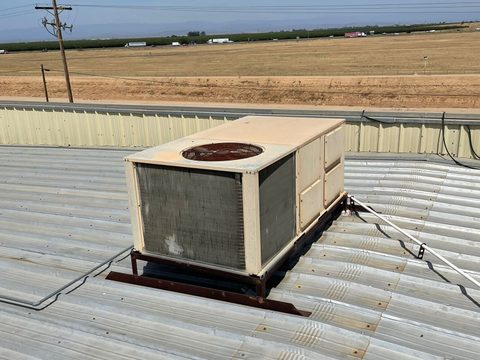 a packaged rooftop air conditioning unit sitting on a corrugated metal roof with an open field behind it